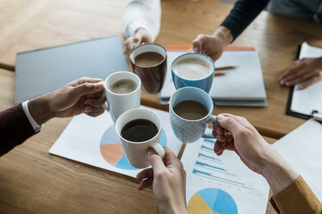 high-angle-people-cheering-with-coffee-mugs-office-meeting